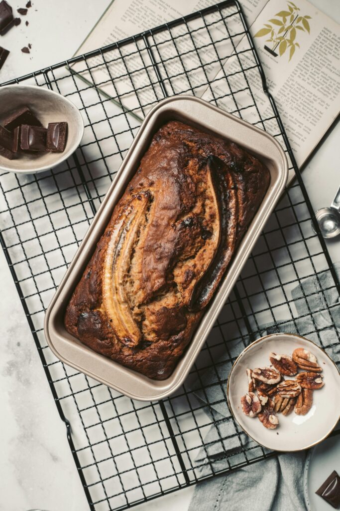 Top view of homemade banana bread in a baking dish on a cooling rack with chocolate and pecans.